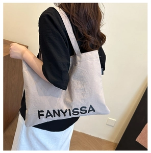 Detail of large beige canvas tote bag with black FANYISSA lettering on shoulder