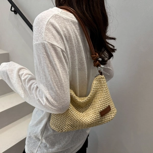 Minimalist beige woven underarm bag with slim brown leather strap worn by a model