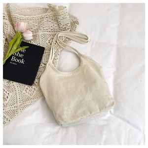 Detail of a creamy lace tote bag on white bedding with pink tulips and a book