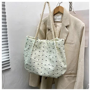 Detail of cream tote bag with black bow prints and unique rope handle on a beige blazer