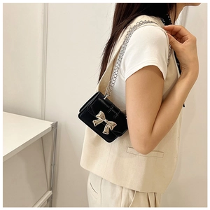 Close-up of black glossy leather mini bag featuring a decorative gold metal bow buckle
