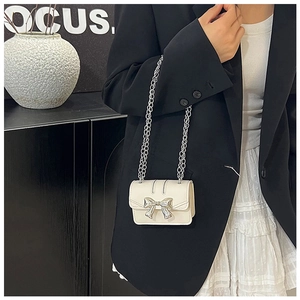 Detail view of mini off-white crossbody bag with large silver metal bow on matte leather
