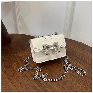 Detail of cream white leather crossbody bag with a large silver metal bow on a wooden table