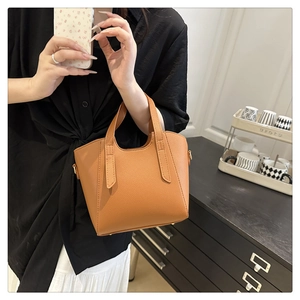 Detail of orange pebble leather bucket bag showing dual handles and metallic hardware
