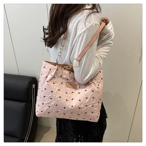 Sac cabas rose matelassé avec motifs nœuds noirs et chaîne dorée porté par un modèle