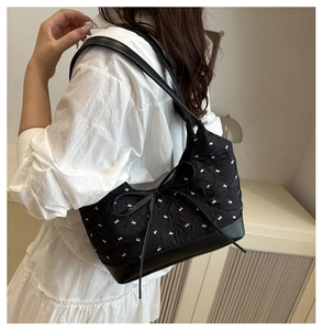 Vista laterale della borsa trapuntata nera con piccoli fiocchi bianchi e grande fiocco decor