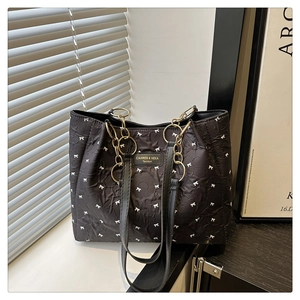 Détail du sac à main matelassé noir avec motifs nœuds blancs et poignée en chaîne dorée