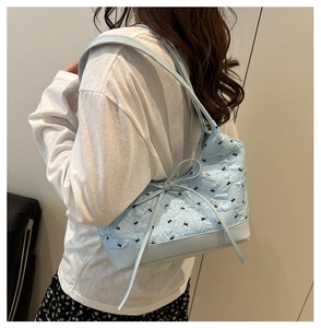 Side view of light blue quilted tote bag with floral patterns and bow detail on model