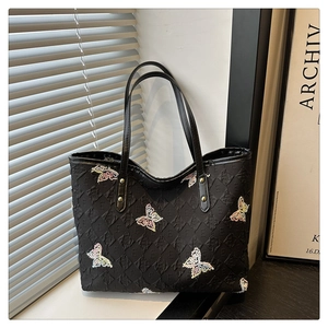 Detail of black quilted tote bag featuring letter E pattern and colorful butterfly embroidery