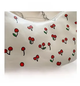 Close-up of a white half-moon bag with red cherry prints and silver chain strap