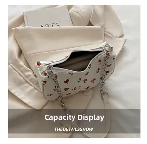 Close-up of cherry print on cream faux leather bag with silver chain strap and zipper