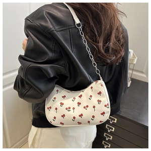 Détail du sac hobo blanc à motifs cerises et chaîne argentée porté par un modèle