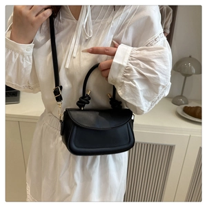Chic black mini crossbody bag with knotted handle and gold hardware on model