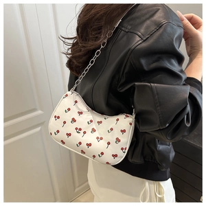 Close-up of white crescent shoulder bag with red cherry prints and silver chain strap