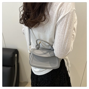 Detail of grey semi-circle flap bag with twisted handle and gold hardware on model
