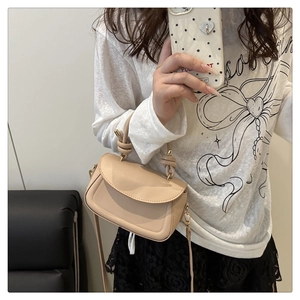 Beige flap crossbody bag with knotted handle and gold metal hardware shown in use