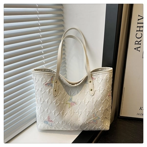 Close-up of butterfly embroidery and embossed letter texture on beige tote bag