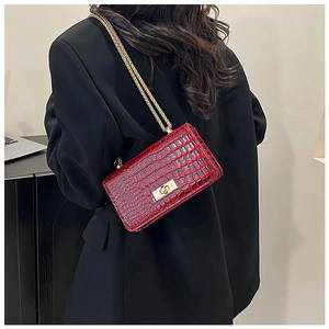 Detail of red crocodile texture crossbody bag with gold chain strap on a black blazer