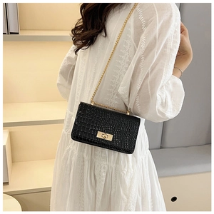 Detail view of a black crocodile pattern chain bag worn by a model in a white dress