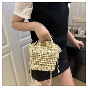 Close-up of beige woven straw bucket bag with drawstring inner liner and shoulder strap