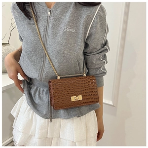 Detail view of glossy brown croc-embossed crossbody bag with golden chain and clasp