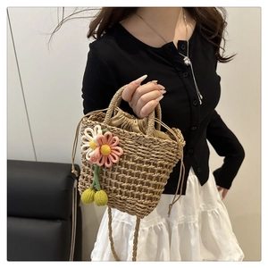 Close-up of woven straw bucket bag with floral accents and cherry charm on model