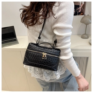 Detail of black woven box crossbody bag with dual golden zippers and adjustable strap