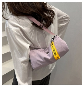 Détail du sac cylindre en nylon violet avec bandoulière rose et sangle à texte jaune
