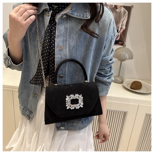 Detail shot of black suede handbag featuring a large crystal buckle and gold chain strap