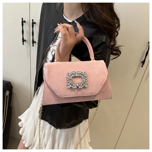 Detail of a pink suede crossbody bag featuring a large sparkling rhinestone buckle and gold chain