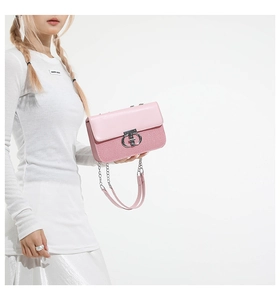 Close-up of pink crossbody bag featuring a silver twist lock and chain strap on a model