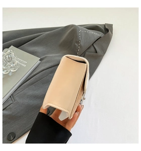 Detail view of cream structured crossbody bag with smooth finish next to a grey blazer