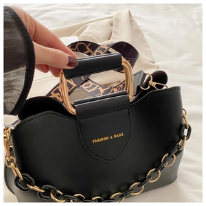 Detail of black handbag with golden chain and branded wide fabric shoulder strap