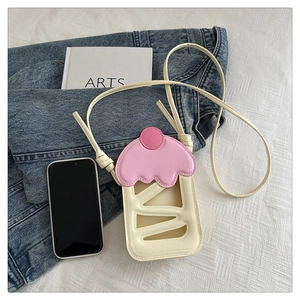 Détail d'un sac de téléphone en forme de cupcake crème et rose sur de la literie blanche