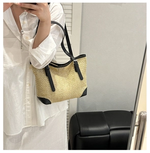 Detail of straw woven tote bag featuring black leather trim and reinforced corner accents