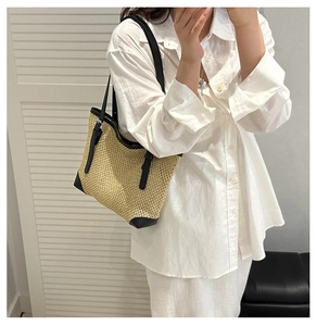 Detail of woven straw tote bag with black leather straps on a white shirt model