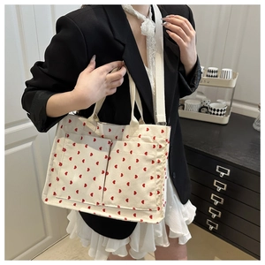 Detailed view of white canvas tote bag featuring red heart patterns and front dual pockets