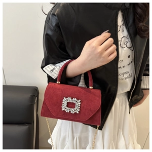 Detail of red suede crossbody bag with a luxury square crystal buckle and gold chain strap
