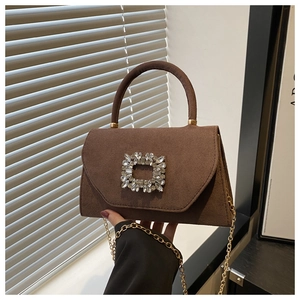 Detail of a brown suede handbag featuring a sparkling crystal buckle and gold chain strap
