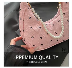 Détail d'un sac hobo plissé rose avec imprimé nœud et anse en perles blanches