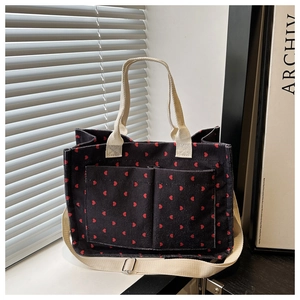 Detailed texture of black corduroy tote bag with red hearts and dual front pockets