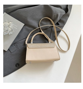 Detailansicht der beigen Pailletten-Handtasche mit Strass-Klappe auf grauem Blazer-Hintergrund
