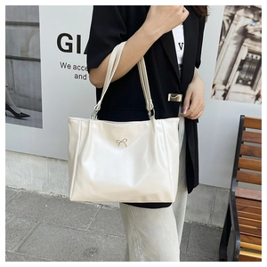 Close-up of a stylish cream tote bag with a silver metal bow and soft PU leather