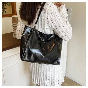 Gros plan du sac cabas noir brillant avec un détail de nœud argenté et grande capacité