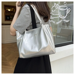 Detail of silver tote bag with metallic bow, pleated texture and unique strap design