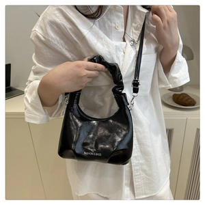 Close-up of black glossy ruched handbag with white fashion text and metallic hardware detail