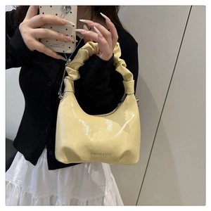 Detail of light yellow patent leather handbag featuring pleated handles and fashion logo