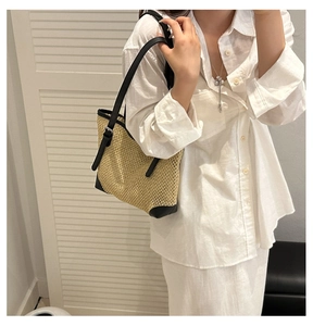 Detailed close-up of straw tote bag showing woven texture and black leather shoulder strap