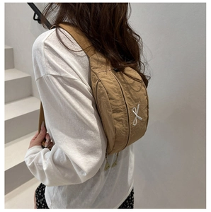 Dettaglio della borsa a tracolla in nylon kaki con ricamo a fiocco bianco e cinturino