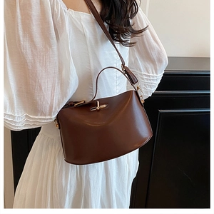 Detail of dark brown leather crossbody bag with golden twist lock on white dress
